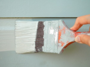 Close up of a paintbrush painting lap siding on a home