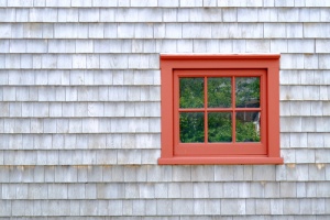 A red window surrounded by aged cedar shingle siding
